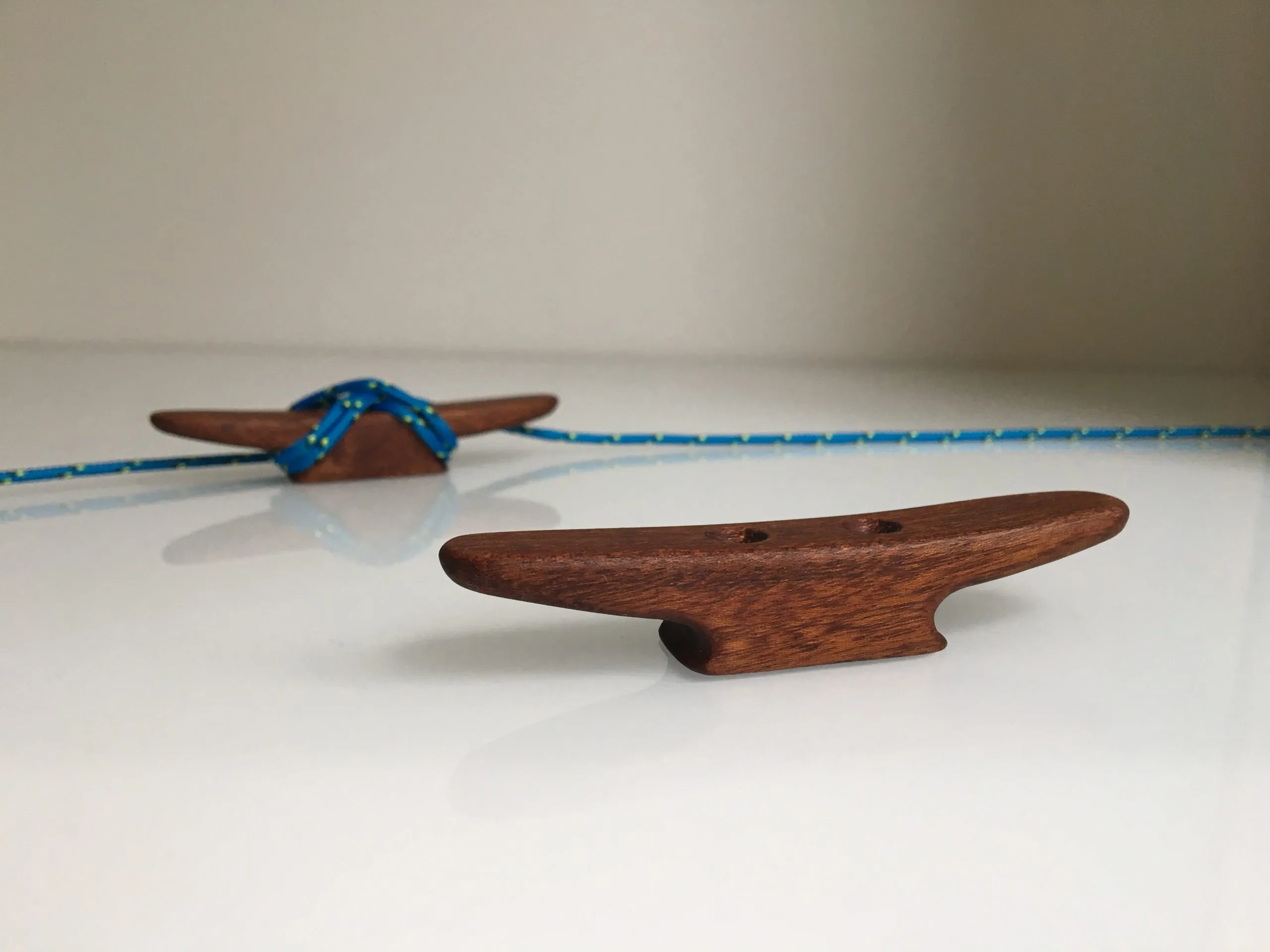 Oiled mahogany mini boat cleat resting on a workbench beside a coil of thin rope