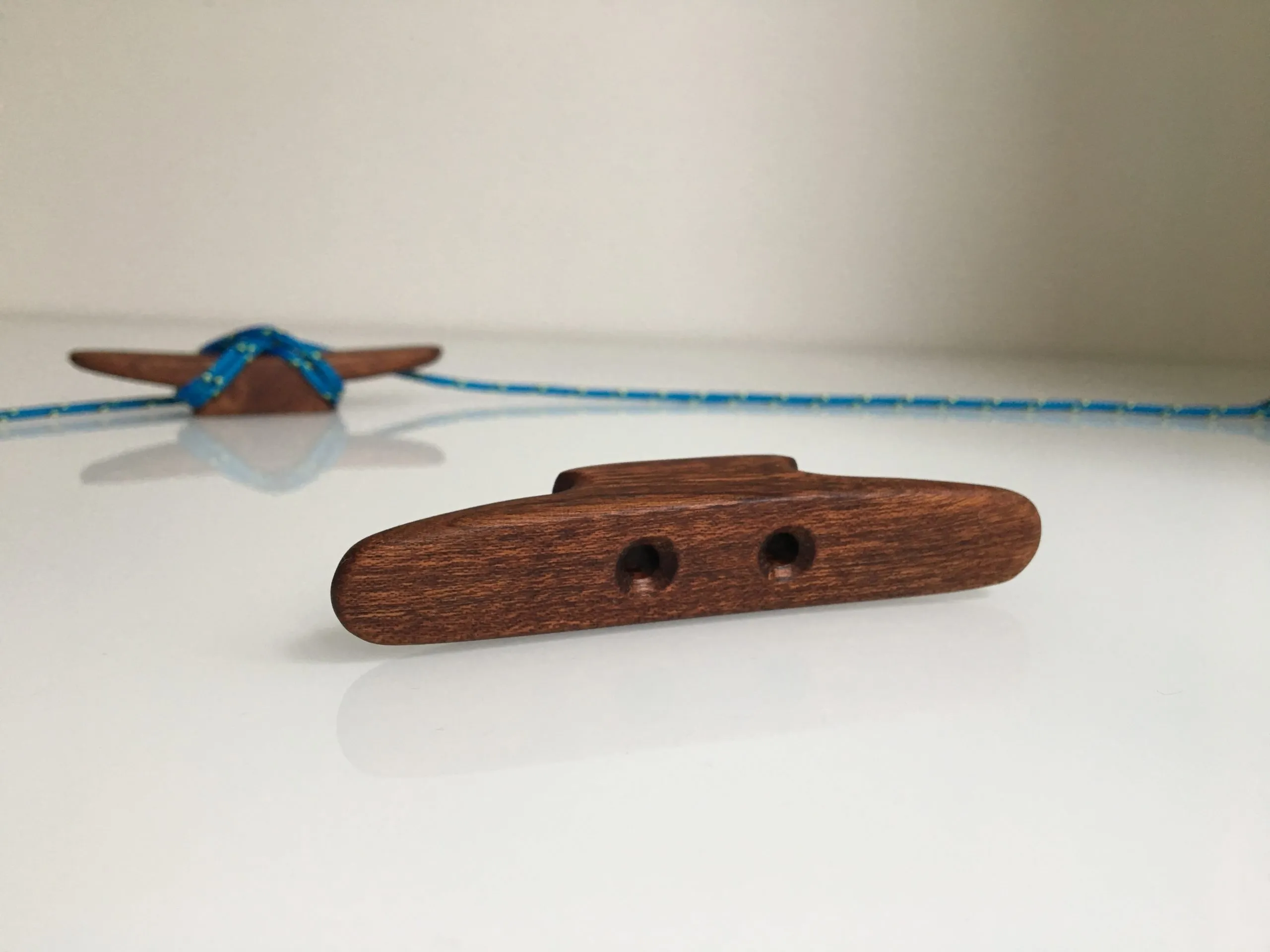 Mahogany mini cleat held between finger and thumb to show its 10cm scale