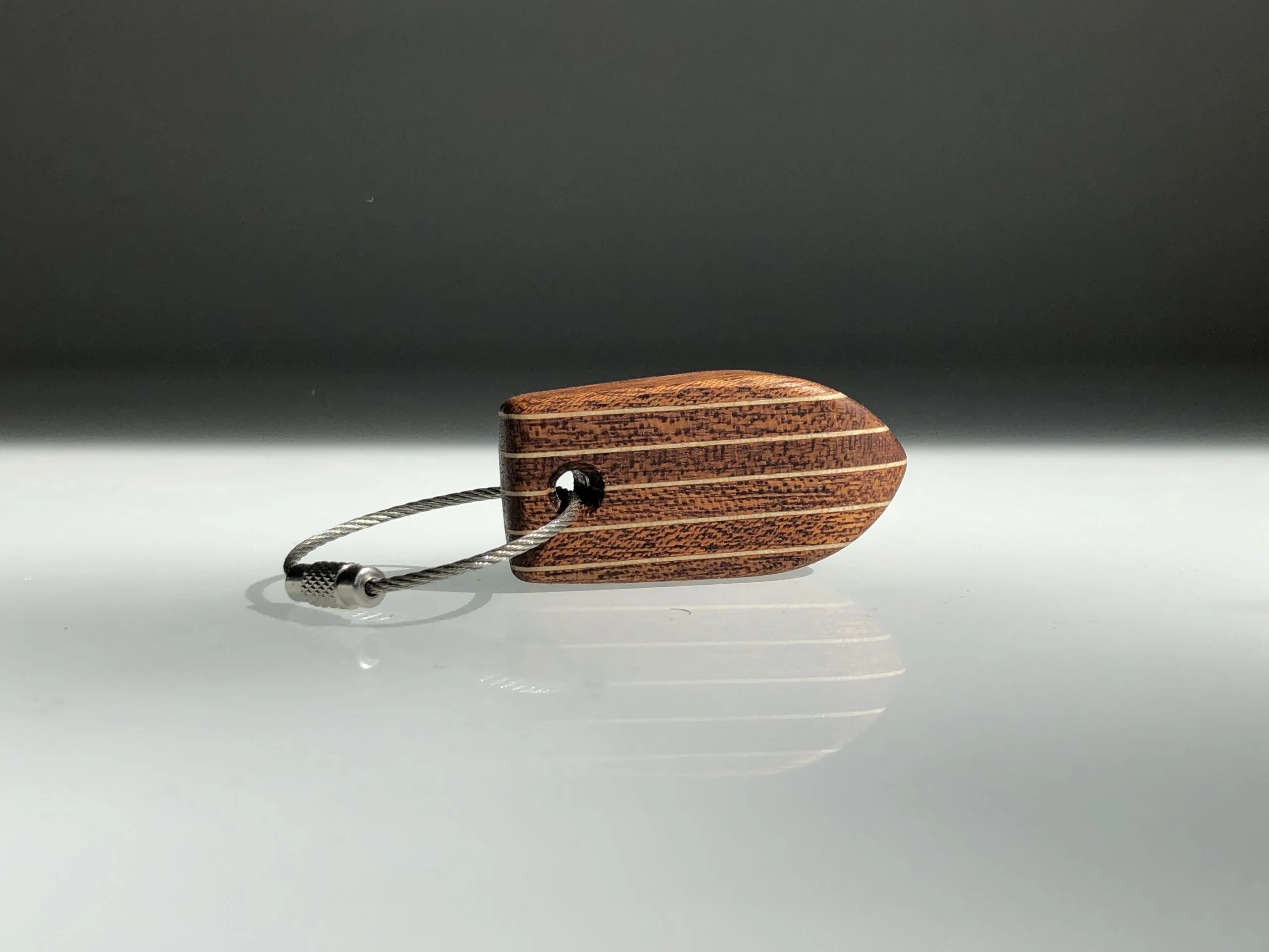 Deck pattern keychain with teak and birch stripes on a dark surface