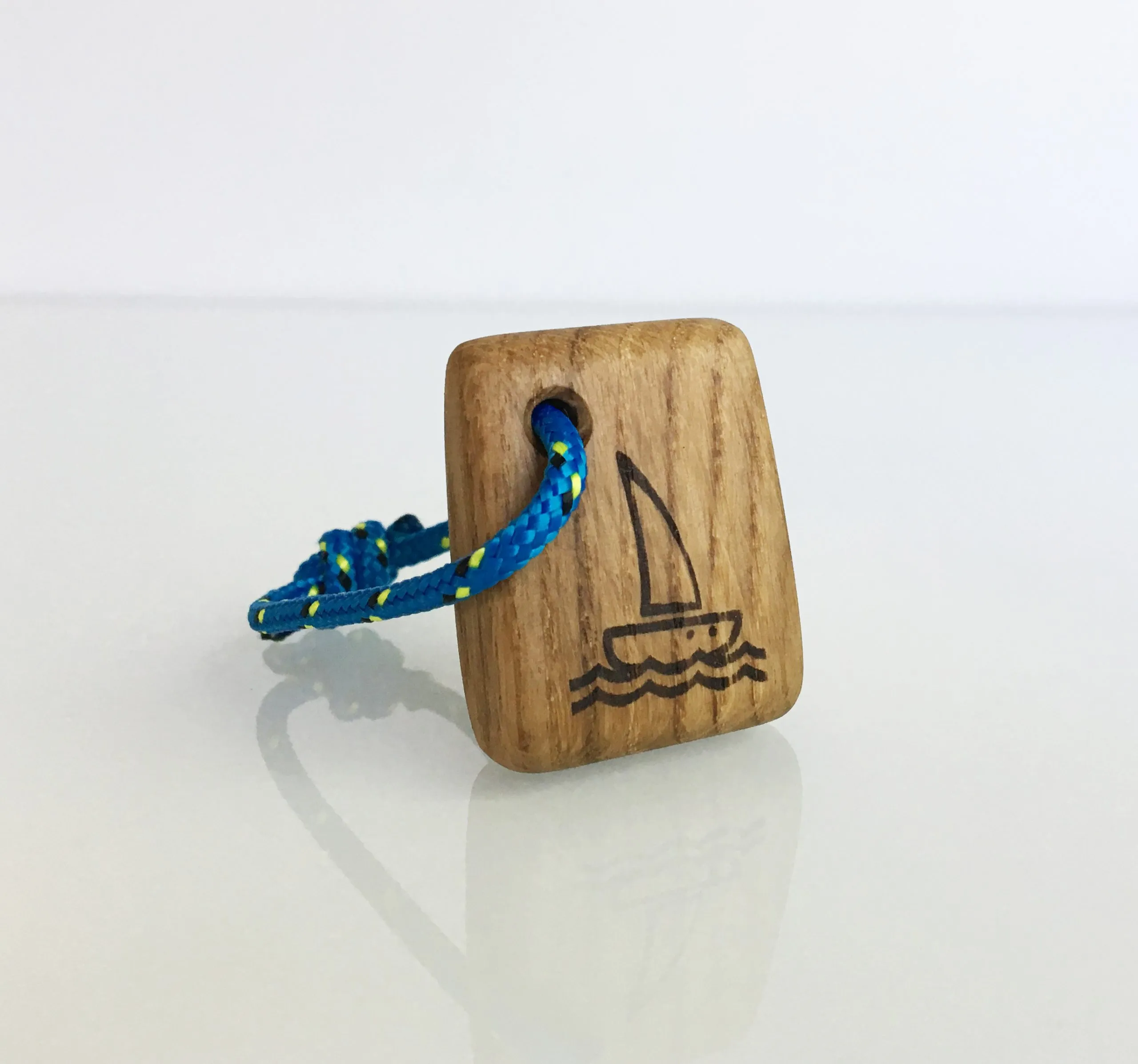 Oak keychain with a burned sailboat emblem hanging from a grey rope loop