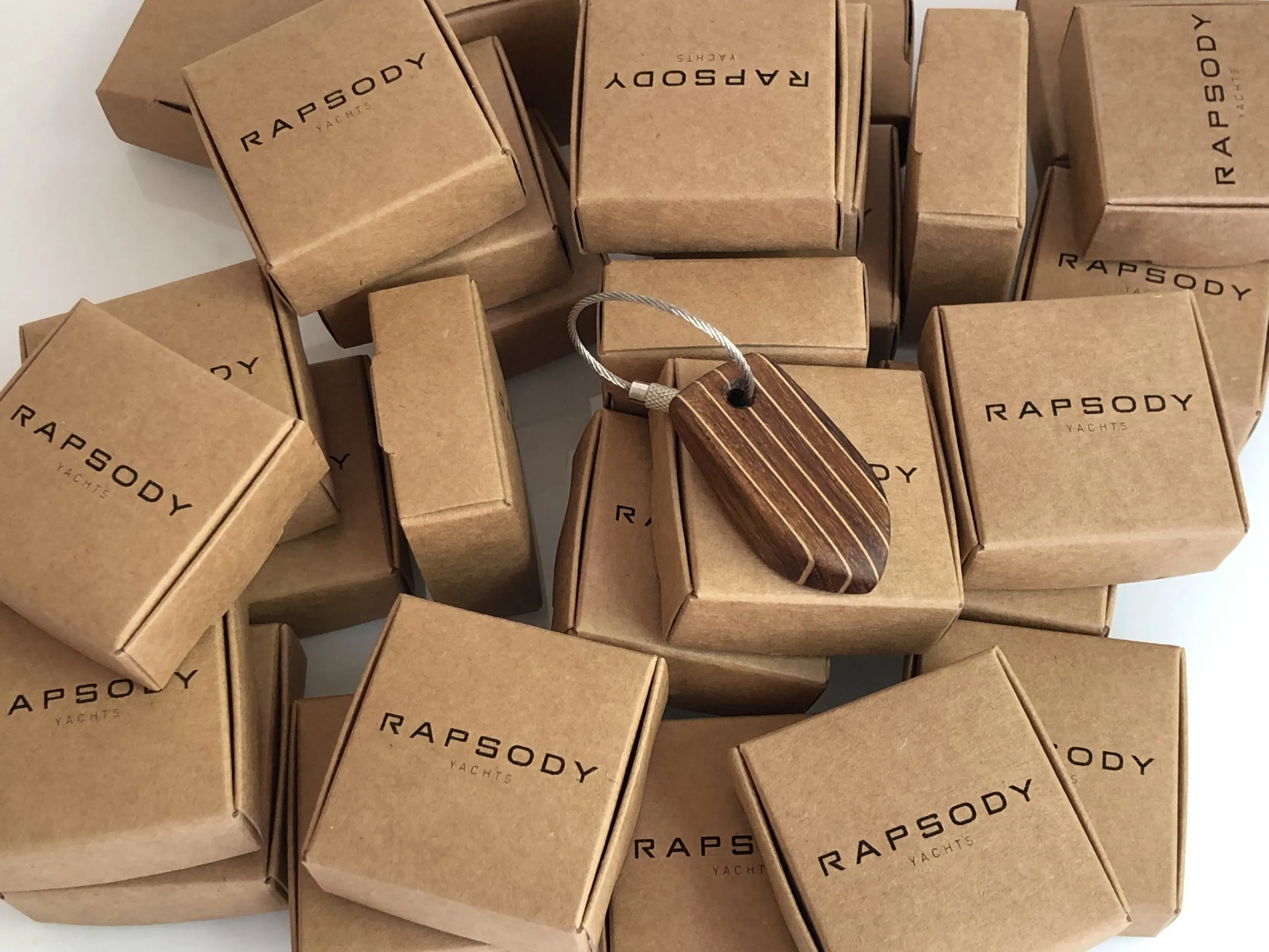 Kraft boxes printed RAPSODY, each holding an engraved teak keychain